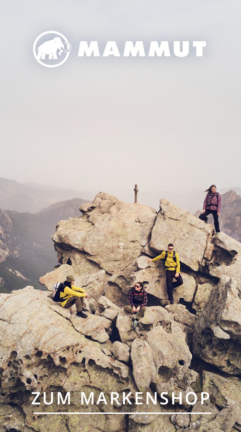 Vier Personen in Outdoor-Ausrüstung sitzen und stehen auf felsigem Gelände mit Bergkulisse im Hintergrund. Der Himmel ist bedeckt. Oben und unten steht „Mammut“ und „Zum Markenshop“.