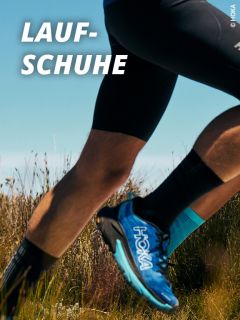 Ein Läufer in schwarzen Shorts und blauen HOKA-Laufschuhen läuft im Freien durch hohes Gras unter blauem Himmel. Der Text "LAUF-SCHUHE" erscheint in fetten weißen Buchstaben in der oberen linken Ecke.