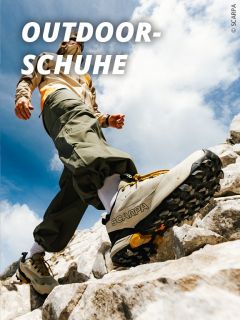 Eine Person mit SCARPA-Wanderschuhen klettert über felsiges Gelände unter blauem Himmel, wobei der Text OUTDOOR-SCHUHE" in fetten weißen Buchstaben oben links erscheint.