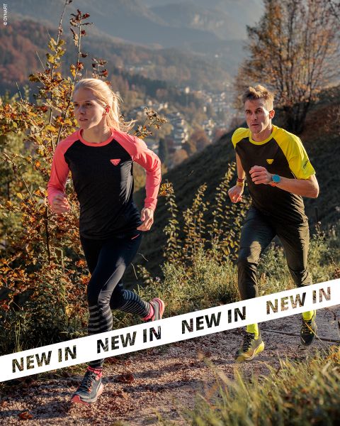 Zwei Personen in Sportkleidung laufen auf einem felsigen Pfad durch eine hügelige, bewaldete Landschaft. Das Sonnenlicht hebt das Herbstlaub hervor. Weiße Banner mit der Aufschrift "NEW IN" in fetten schwarzen Buchstaben durchziehen den unteren Teil des Bildes.