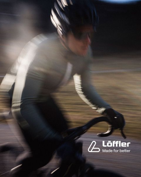 Zwei Mountainbiker fahren auf einem felsigen Trail inmitten üppiger Vegetation. Beide tragen Helme und Sonnenbrillen. In der unteren rechten Ecke ist der Schriftzug „Löffler Made for better“ zu sehen.