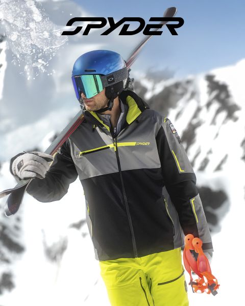 Ein Skifahrer in schwarz-gelbem Outfit fährt einen schneebedeckten Hang hinunter, im Hintergrund eine schneebedeckte Landschaft. Oben steht der Text: „SPYDER FÜR SKIFAHRER SEIT 1978.“ In der unteren rechten Ecke ist ein kleines weißes Spinnenlogo zu sehen.