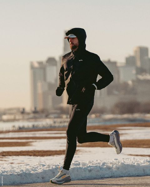 Eine Person in Sportkleidung joggt an einem klaren Tag über einen verschneiten Weg mit der Skyline der Stadt im Hintergrund.