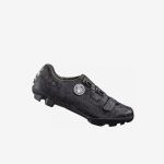 Ein schwarzer Fahrradschuh mit strukturiertem, camoähnlichem Muster, einem Ziffernblatt-Verschlusssystem und einer robusten Sohle, die für den Einsatz im Gelände konzipiert ist.