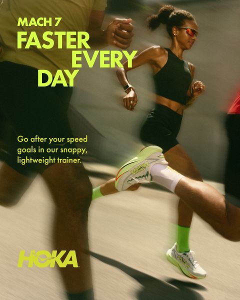 Zwei Läufer, ein Mann und eine Frau, laufen einen felsigen Bergpfad hinauf, umgeben von üppigem Grün und hohen Bäumen. Beide tragen Laufkleidung und Trinkrucksäcke. Oben prangt deutlich das Wort „HOKA“. Im Hintergrund erheben sich schneebedeckte Berge.