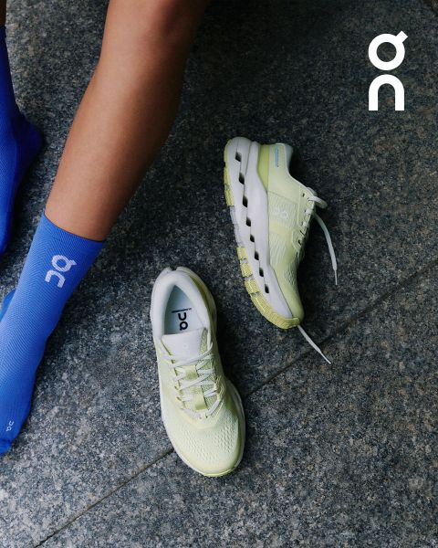 Eine Person in hellblauen Socken neben einem Paar hellgelber ON-Laufschuhe auf einem grauen Steinboden, mit dem ON-Logo in der oberen rechten Ecke.