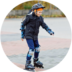 Ein Kind mit Helm, Knie- und Ellbogenschützern und Rollschuhen fährt im Freien auf einer gepflasterten Fläche Rollschuh, lächelt und schaut nach unten, um das Gleichgewicht zu halten.