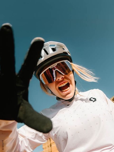 Ein lächelnder Radfahrer mit Helm, Sonnenbrille und Handschuhen streckt sich vor einem strahlend blauen Himmel in die Kamera.