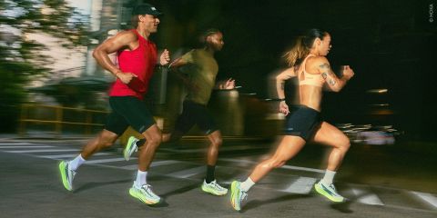Drei Läufer in Sportbekleidung sprinten nachts eine Stadtstraße entlang; sie wurden in Bewegung mit unscharfem Hintergrund eingefangen.