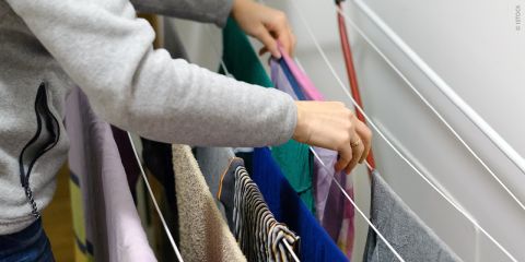 Eine Person hängt Wäsche auf einem Wäscheständer im Haus auf und ordnet Kleidung und Handtücher von Hand an.