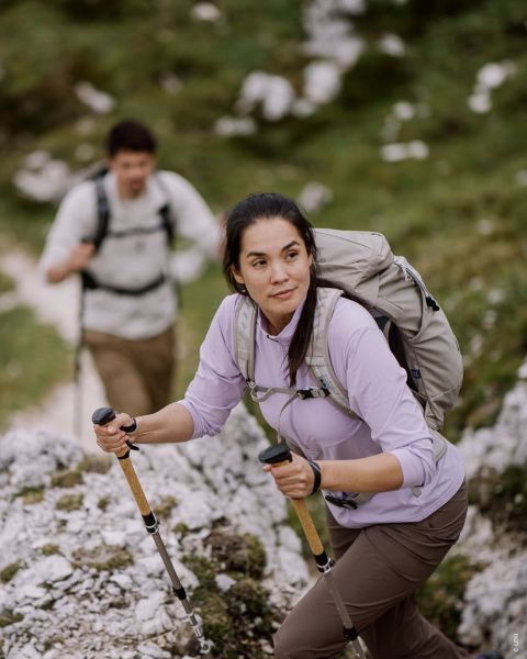 Zwei Bilder auf Holzhintergrund zeigen ein weibliches und ein männliches Model in Outdoor-Wanderkleidung. Das weibliche Model trägt ein rosa-grünes Outfit, das männliche Model ein grünes Outfit und hält Trekkingstöcke in der Hand. Text: „OUTDOOR-TYP AKTIVWANDERER“.