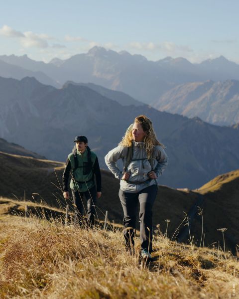 Zwei Personen sind auf separaten Fotos zu sehen. Das linke Foto zeigt eine Person in Wanderkleidung mit Trekkingstöcken, das rechte eine weitere Person mit Rucksack und Jacke. Der Hintergrund ist eine Holzstruktur mit Moos. Der Text lautet „Outdoor-Typ Genusswanderer“.