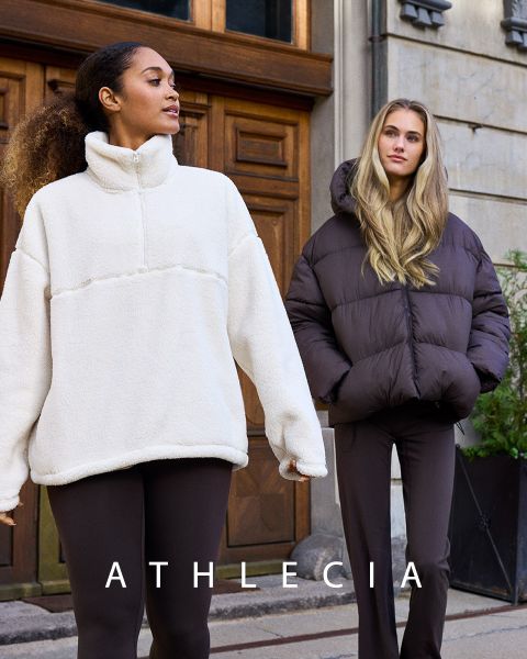 Zwei Frauen in blauer Athlecia-Sportbekleidung posieren auf felsigem Gelände. Eine trägt Sweatshirt und Shorts, die andere ein weißes Crop-Top und blaue Hosen. Über ihnen ist der Markenname „Athlecia“ zu sehen.
