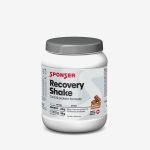 Ein weißer Behälter mit „Sponser Recovery Shake“ im Schokoladengeschmack, auf dem die Nährwertangaben zu sehen sind, sowie ein grauer Deckel vor einem einfarbigen Hintergrund.